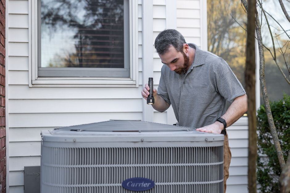A technician inspecting an outdoor air conditioner beside a house