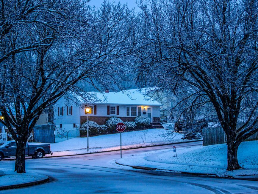 A suburban home on a snowy evening with a lit window and street lights